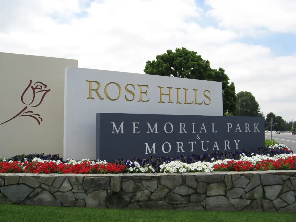 Monument sign at Rose Hills Memorial Park entrance with decorative flowers at the base