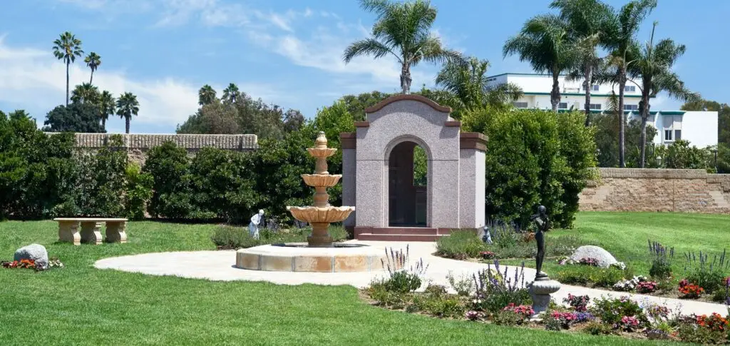 A serene view of the fountain and mausoleum at Ivy Lawn Memorial Park, surrounded by lush greenery and vibrant flowers.