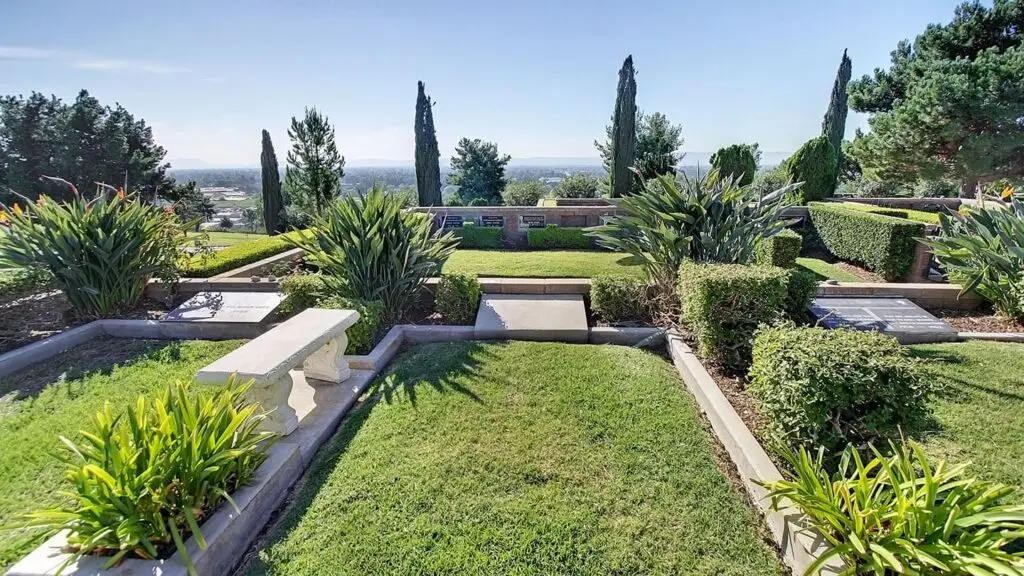 A peaceful landscape view at Eden Memorial Park, featuring lush greenery, engraved memorials, and a stone bench for reflection.