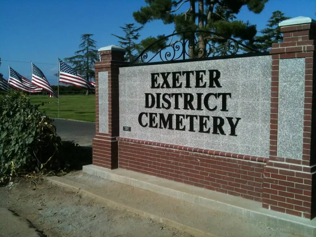 Entrance sign of Exeter District Cemetery in Exeter, CA, with American flags in the background, representing a peaceful and honored resting place.