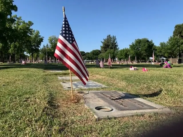 American flag placed next to a bronze headstone at Kern County Cemetery District, honoring veterans.