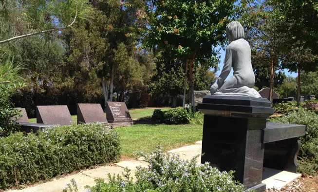 A peaceful sculpture at Loma Vista Memorial Park surrounded by engraved granite headstones.