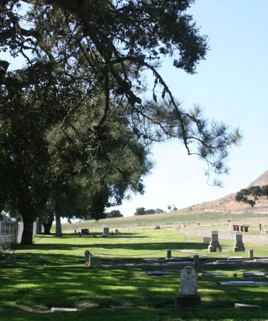 Scenic view of Los Alamos Cemetery District with lush greenery and historic grave markers under shaded trees.