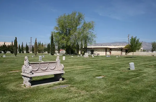 Peaceful landscape at Mojave Cemetery featuring a carved stone bench and memorial headstones under a blue sky.