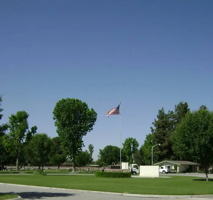 A peaceful landscape view of Shafter Memorial Park featuring a waving American flag, lush greenery, and a serene cemetery setting.