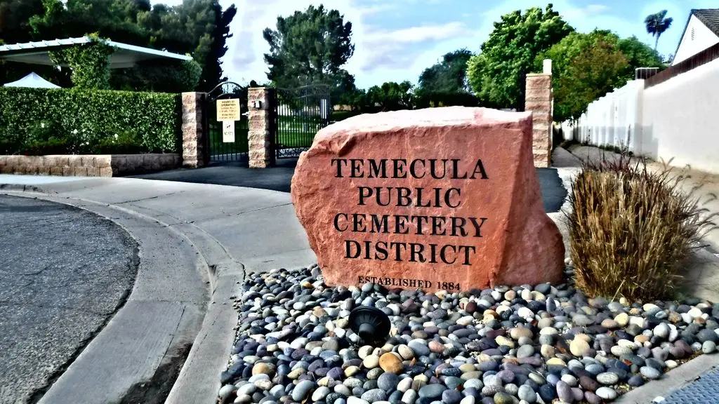 Entrance of Temecula Public Cemetery District with a large engraved stone sign, surrounded by landscaping and a gated entrance.