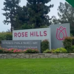 Main entrance sign at Rose Hills Memorial Park in Whittier, California, surrounded by greenery and flowers