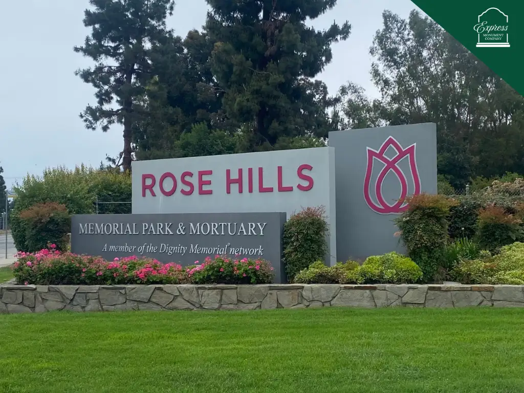 Main entrance sign at Rose Hills Memorial Park in Whittier, California, surrounded by greenery and flowers